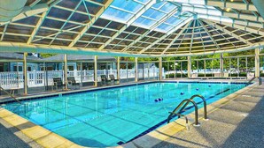A swimming pool with a glass ceiling, lounge chairs, and a fenced deck area.