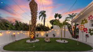 A landscaped garden with palm trees, a rock centerpiece, and string lights. - Hippie House-5 bedroom, Sleeps 12! Pool, Basketball, Mini golf, Pickleball Ct! (Bradenton)