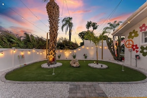 A landscaped garden with palm trees, a rock centerpiece, and string lights. - Unique and FUN 5-bedroom house with Pool, Basketball, Mini golf, Pickleball Ct! (Bradenton)