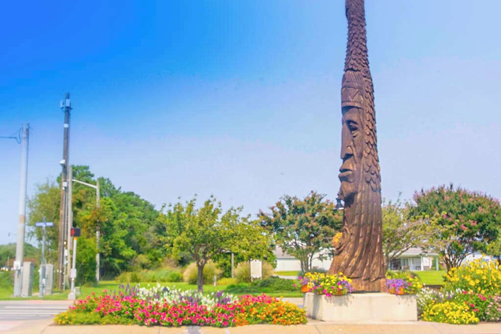 A tall, textured sculpture in a landscaped area with flowering plants.