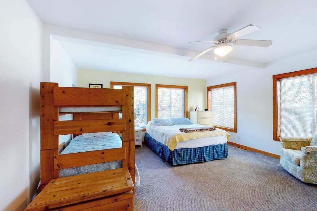 A bedroom with a bunk bed, a single bed, a ceiling fan, and large windows.