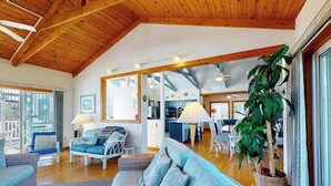 En rummelig opholdsstue med højt til loftet, stor sofa, spisebord og en potteplante.