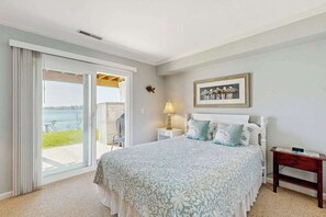 A bedroom with a large bed, a nightstand, a lamp, a framed picture, and a view of the outdoors. - Salt Pond townhouse overlooking the water with WiFi & washer/dryer (Bethany Beach)