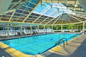 A swimming pool with a glass roof, surrounded by lounge chairs and a white fence. - Salt Pond townhouse overlooking the water with WiFi & washer/dryer (Bethany Beach)