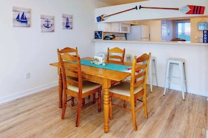 A dining area with a wooden table and chairs, a kitchen area with white cabinets, and a view of the outside. - Bayberry Woods condo with fast WiFi, on-site pool, tennis & pickleball (Bethany Beach)