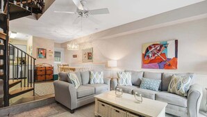 A modern living room with a grey sofa, a coffee table, a ceiling fan, and a staircase. - Sea Pines Village Beach House with Fast WiFi, Full Kitchen, A/C, & a Shared Pool (Bethany Beach)