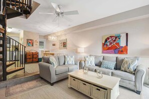 Ein modernes Wohnzimmer mit einem grauen Sofa, einem Couchtisch, einem Deckenventilator und einer Treppe.