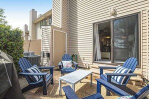 Eine Terrasse im Freien mit Adirondack-Stühlen, einem Tisch und einem Grill.