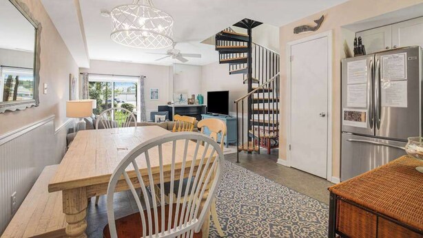 A dining area with a wooden table and chairs, a chandelier, a spiral staircase, and a refrigerator. - Sea Pines Village Beach House with Fast WiFi, Full Kitchen, A/C, & a Shared Pool (Bethany Beach)