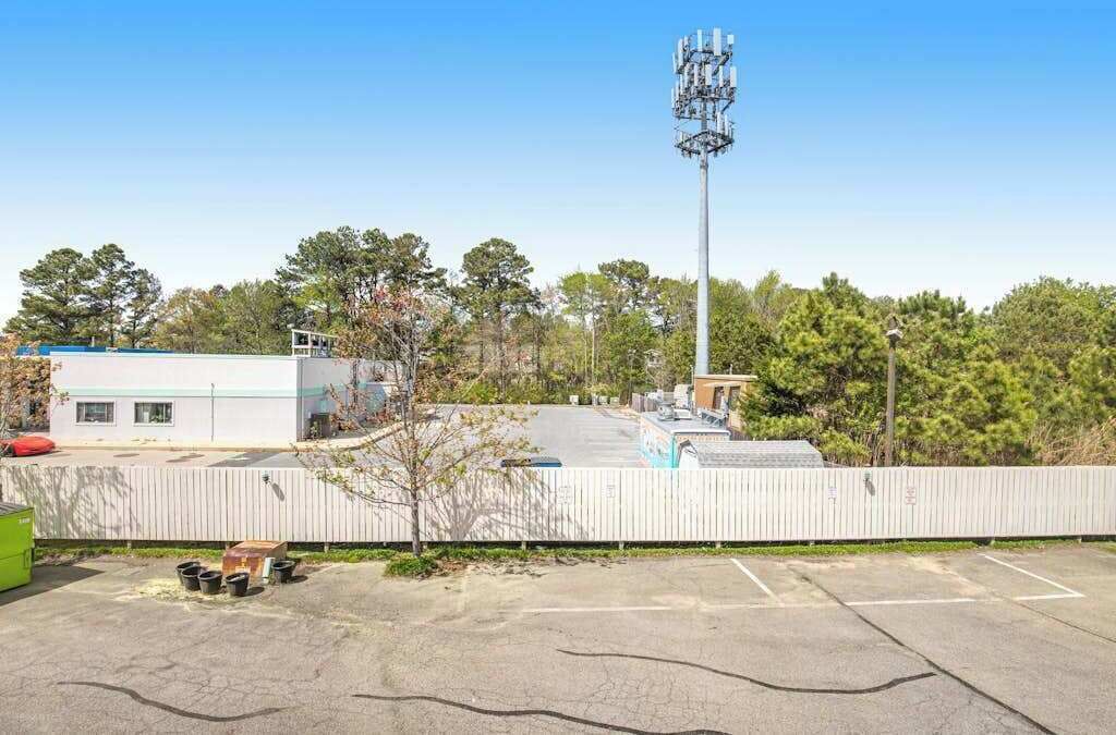 A parking lot with a fenced area, a building with a flat roof, and a tall communication tower.