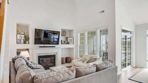 A living room with a sofa, television, fireplace, and a view of the outside. - Bear Trap Dunes townhome with central AC & washer/dryer - on-site pools & tennis (Ocean View)