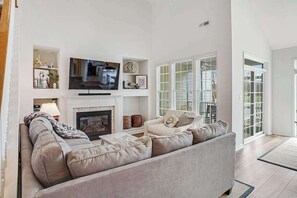 A living room with a sofa, television, fireplace, and a view of the outside. - Bear Trap Dunes townhome with central AC & washer/dryer - on-site pools & tennis (Ocean View)