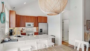 A modern kitchen with wooden cabinets, a marble island, white chairs, and a large woven light fixture. - Bear Trap Dunes townhome with central AC & washer/dryer - on-site pools & tennis (Ocean View)