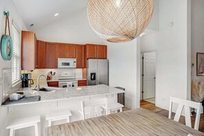 A modern kitchen with wooden cabinets, a marble island, white chairs, and a large woven light fixture. - Bear Trap Dunes townhome with central AC & washer/dryer - on-site pools & tennis (Ocean View)