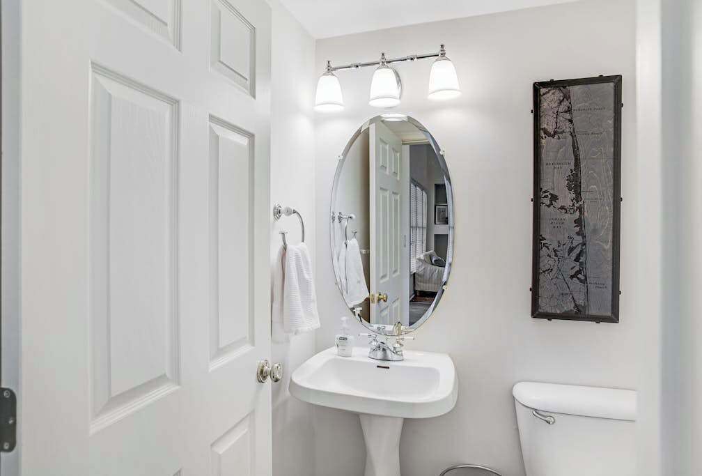 Une salle de bain avec un lavabo blanc, un miroir, des toilettes et une carte encadrée accrochée au mur.