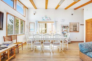 A dining area with a table and chairs, a bookshelf, and a window with blinds. - Fenwick Island spacious beach house with deck, W/D & full kitchen - dog-friendly (Fenwick Island)