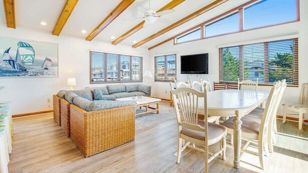 A spacious living area with a sofa, dining table, and chairs, large windows, and a ceiling fan. - Fenwick Island spacious beach house with deck, W/D & full kitchen - dog-friendly (Fenwick Island)