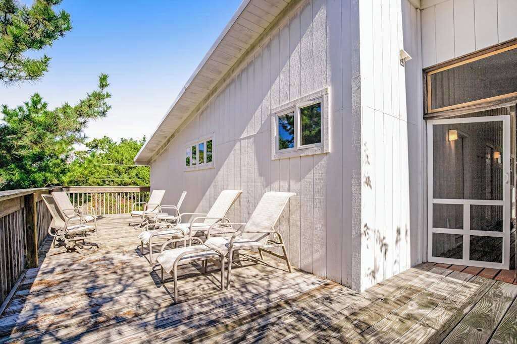 A deck with sun loungers and a white building with windows and a sliding glass door.