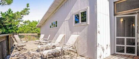 A deck with sun loungers and a white building with windows and a sliding glass door.