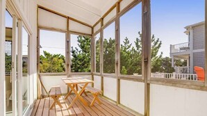 A covered outdoor area with a wooden table and benches, large windows, and a view of trees and a neighboring building. - Fenwick Island spacious beach house with deck, W/D & full kitchen - dog-friendly (Fenwick Island)