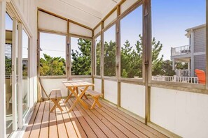 A covered outdoor area with a wooden table and benches, large windows, and a view of trees and a neighboring building. - Fenwick Island spacious beach house with deck, W/D & full kitchen - dog-friendly (Fenwick Island)