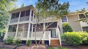 Una casa de dos pisos con balcón, un porche pequeño y un jardín cuidado.