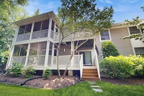 A two-story house with a balcony, a small porch, and a well-maintained garden. - Corner Sea Colony condo with screened porch, pools, hot tub & tennis (Bethany Beach)