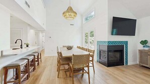 Un comedor amplio con una mesa larga y sillas, una cocina con encimera blanca, y una chimenea con revestimiento de azulejos.