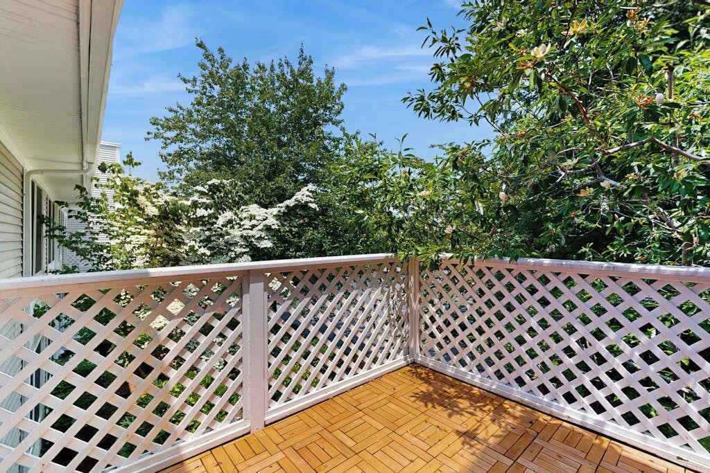 A wooden deck with a white lattice railing, surrounded by trees and a building.
