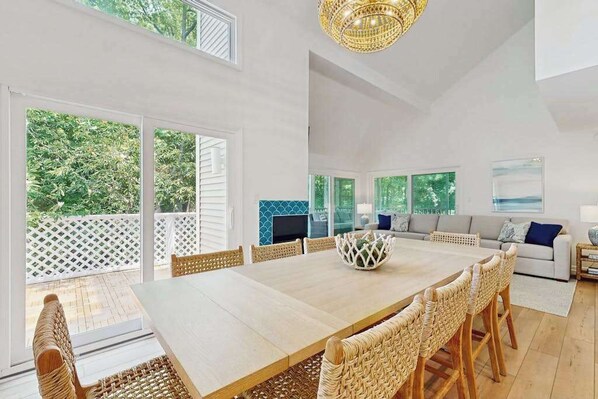 A spacious living area with a large dining table, wicker chairs, a sofa, and a TV. - Corner Sea Colony condo with screened porch, pools, hot tub & tennis (Bethany Beach)