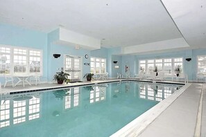 Ein Innenpool mit klarem, blauem Wasser, umgeben von weißen Stühlen und Tischen, mit großen Fenstern für natürliches Licht.