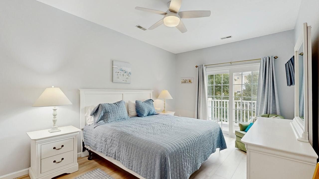 A bedroom with a bed, nightstands, a ceiling fan, and a window with curtains.