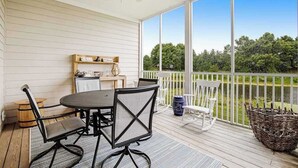 Eine überdachte Terrasse mit Tisch und Stühlen, einem Deckenventilator und Blick auf Grünflächen.