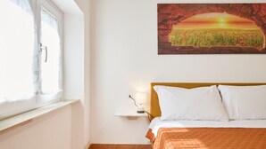 A bedroom with a bed, a nightstand, a lamp, a window with curtains, and a painting of a sunset over a field. - Apartment 'La Casa Di Mia' in Piombino (Piombino)