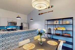A modern kitchen with a blue and white patterned backsplash, a dining table with placemats, and a bookshelf with board games. - Sea Colony townhome with large deck, fast WiFi & central AC - fully renovated (Bethany Beach)