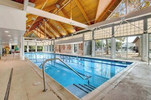 An indoor swimming pool with a wooden ceiling, large windows, and a clear view of the outside. - Bear Trap Dunes condo with access to tennis/pickleball, sauna, pool & fast WiFi (Ocean View)
