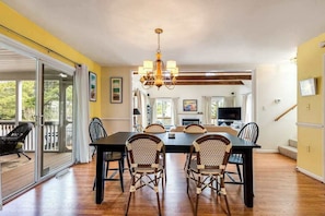 Un coin repas avec une table et des chaises, un lustre et une vue sur l’extérieur, visible à travers une porte vitrée.