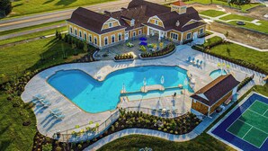 A large swimming pool with a sunken center, surrounded by lounge chairs and umbrellas, with a tennis court and a building with a sloped roof. - Ocean View Beach Club stylish home with outdoor pool, fast WiFi, & wet bar (Ocean View)