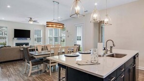 A modern kitchen with a central island, pendant lighting, and a dining area with a sofa and chairs. - Ocean View Beach Club stylish home with outdoor pool, fast WiFi, & wet bar (Ocean View)