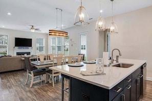 A modern kitchen with a central island, pendant lighting, and a dining area with a sofa and chairs. - Ocean View Beach Club stylish home with outdoor pool, fast WiFi, & wet bar (Ocean View)