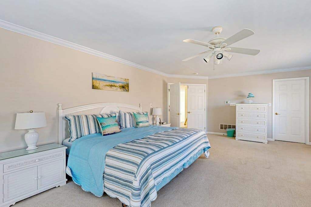 A bedroom with a bed, nightstands, a dresser, a ceiling fan, and a door.
