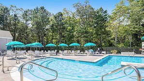 Una piscina con sillas de descanso y sombrillas, rodeada de árboles.