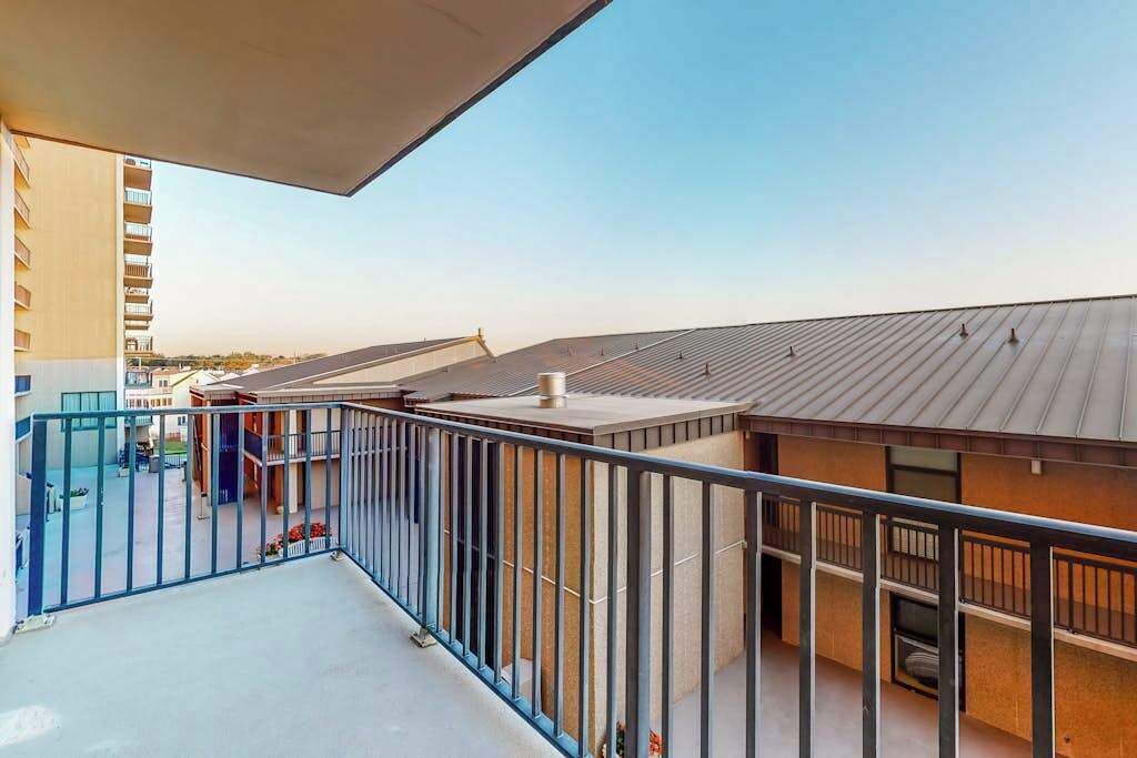 A balcony with a metal railing, a view of a building with a sloped roof, and a clear sky.