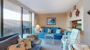 Un salon moderne avec un canapé, des fauteuils, une table basse et une grande fenêtre donnant sur un balcon.