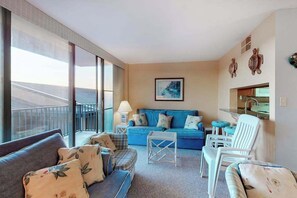 A modern living room with a sofa, chairs, a coffee table, and a large window with a balcony view. - Sea Colony oceanfront 3rd floor condo w/ free WiFi, shared sauna, & tennis court (Bethany Beach)