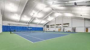 Un court de tennis intérieur doté d’un filet, d’un revêtement de sol vert et d’une zone de jeu bleue.