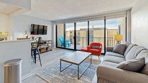 Ein modernes Wohnzimmer mit Sofa, Couchtisch, Wandfernseher und Balkon mit Sitzgelegenheit.