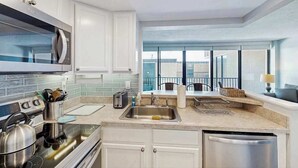 Eine moderne Küche mit Edelstahlgeräten, einer eingebauten Mikrowelle und einem großen Fenster mit Blick auf einen Balkon.