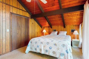 Ein Schlafzimmer mit Holzbalkendecke, einem Bett mit floralem Überwurf, zwei Nachttischlampen und einem Nachttisch.