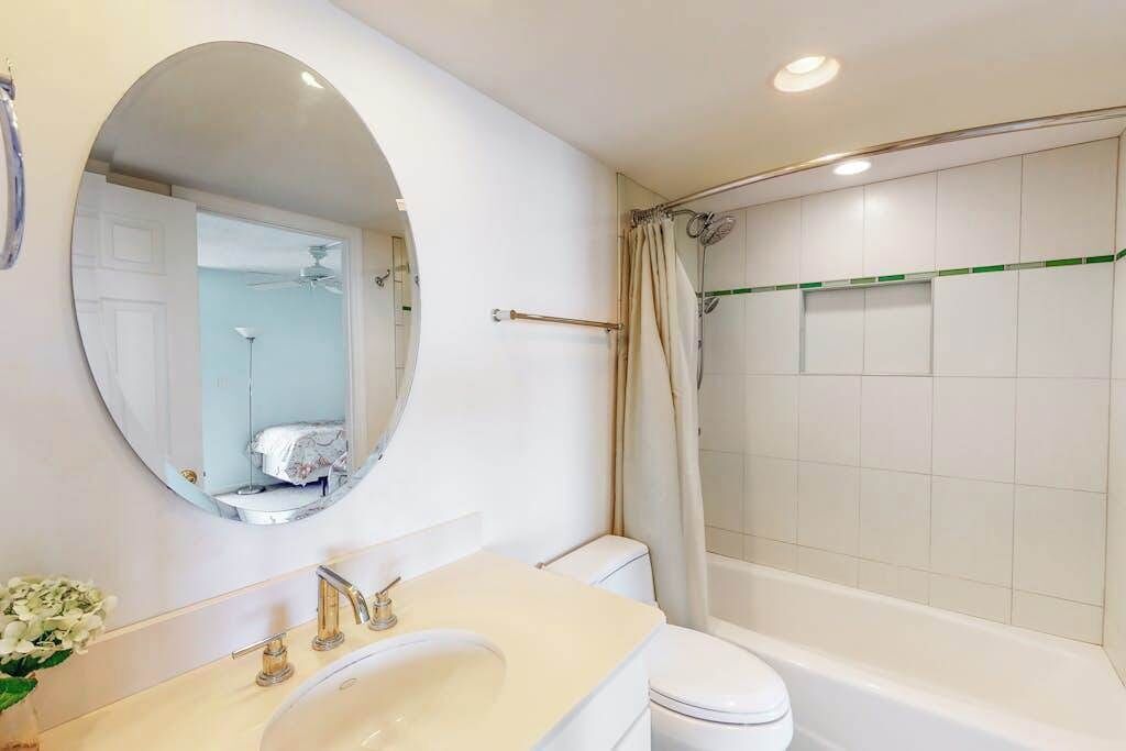 Un bagno con uno specchio rotondo, un lavandino, un water e una zona doccia.